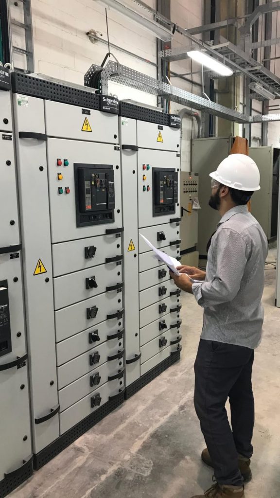 Profissional consultando informações técnicas diante de painéis elétricos.