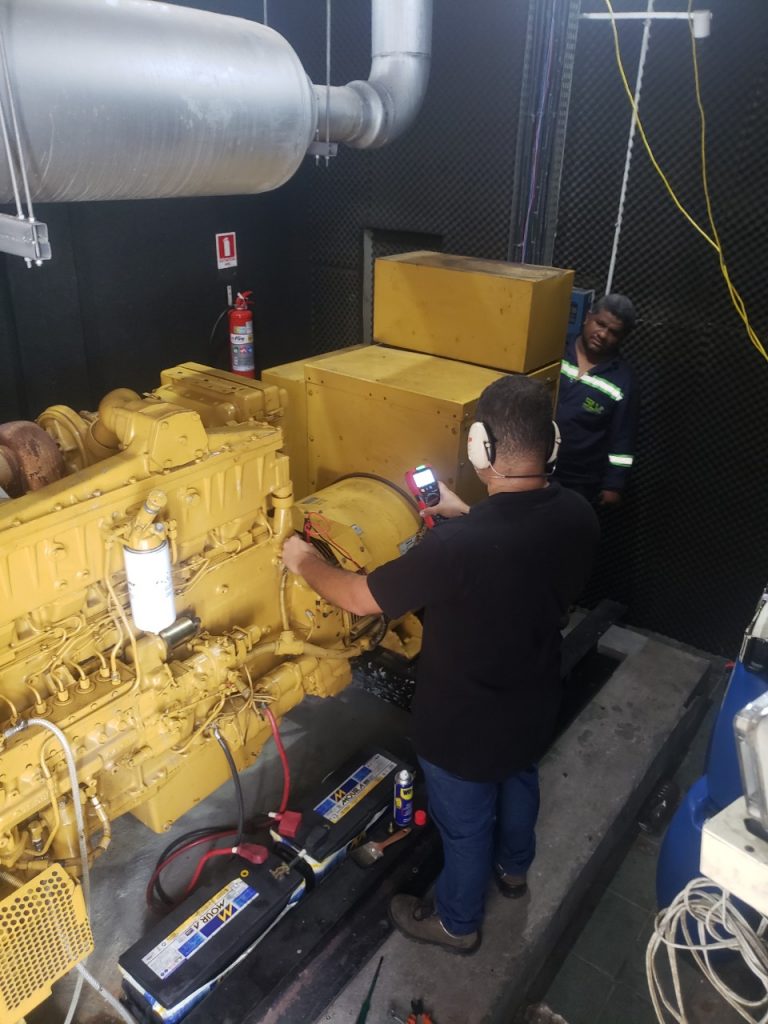Técnico realizando manutenção junto ao motor de um grupo gerador.